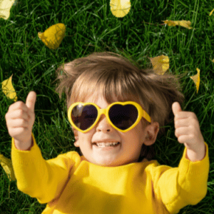 Усмихнато дете с жълта блузка лежи на тревата и с вдигнати ръчички