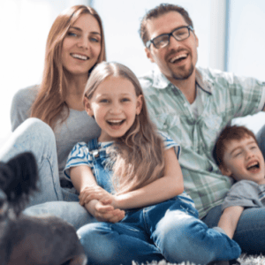 Щастливо семейство с 2 деца и куче, усмихнати, седнали на диван